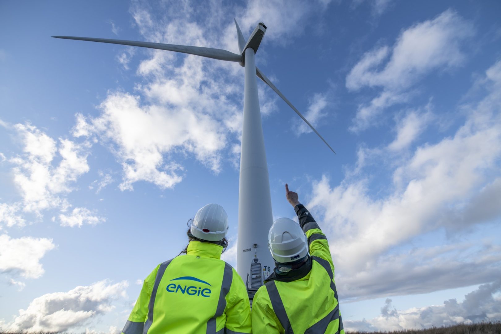 Two ENGIE employees pointing up at wind turbine