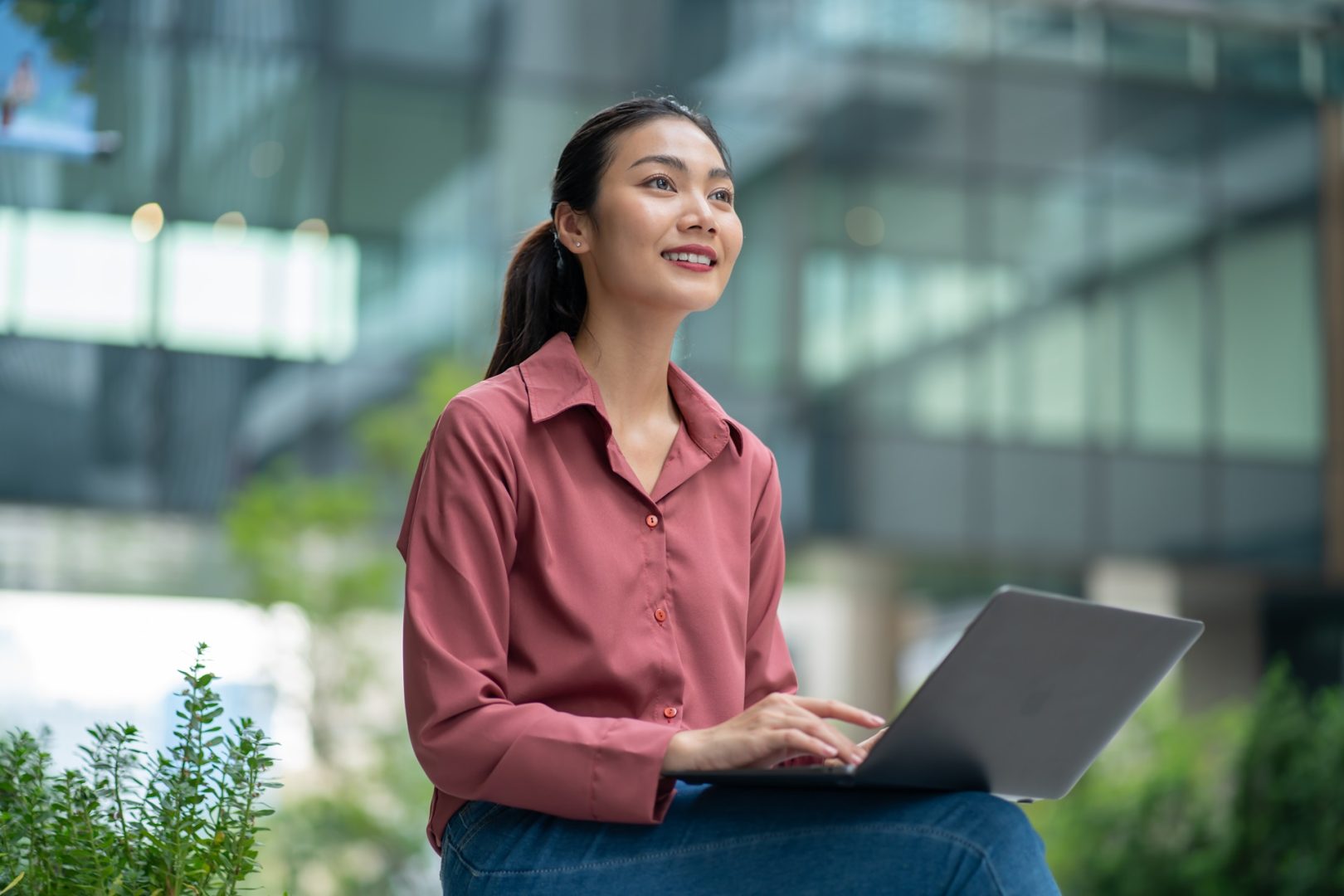Business women working on laptop outdoors with green city background