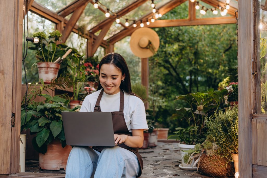 Happy shop owner with laptop by doors of greenhouse