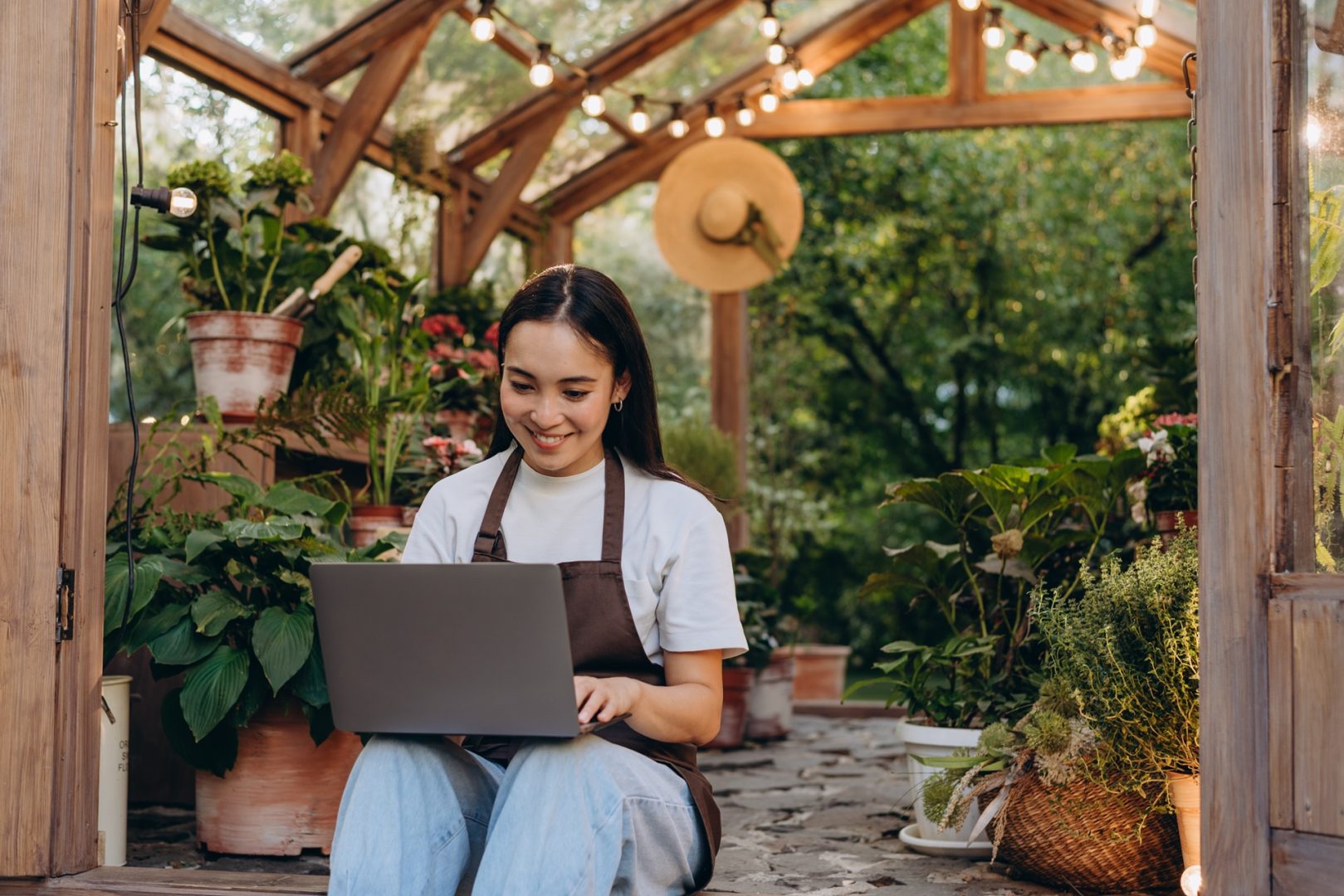 Happy shop owner with laptop by doors of greenhouse